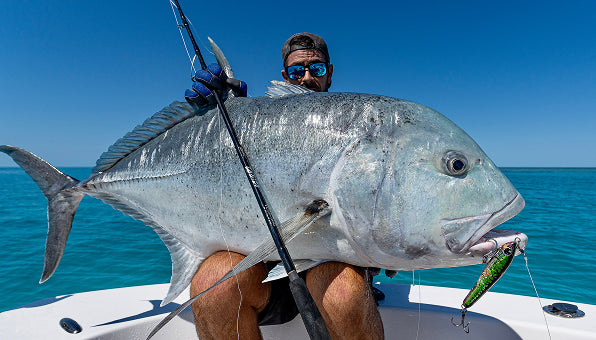 Jonny Brooks holding a giant trevally across the bow, blue mirror lenses